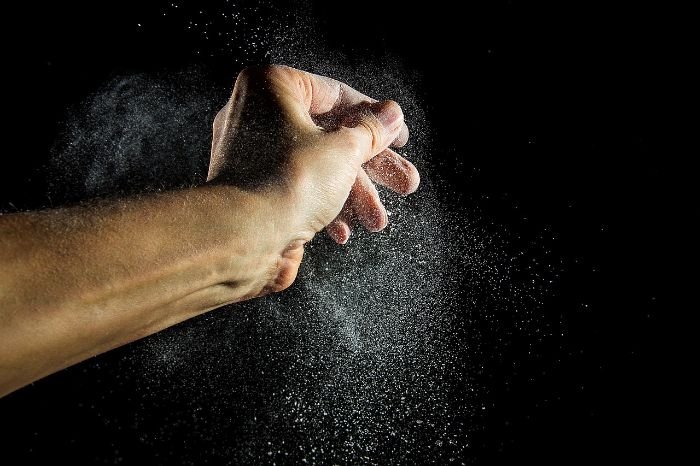A close-up image capturing the dynamic motion of fine particles being released from a person's hands, symbolizing the composition of house dust which includes a variety of microscopic elements, not just human skin.