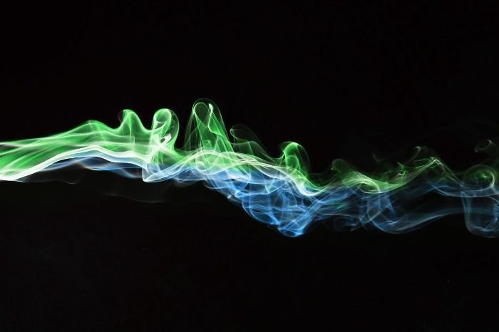 Streaks of green and blue smoke against a black background, symbolizing the movement of air and the importance of maximizing airflow in indoor environments.
