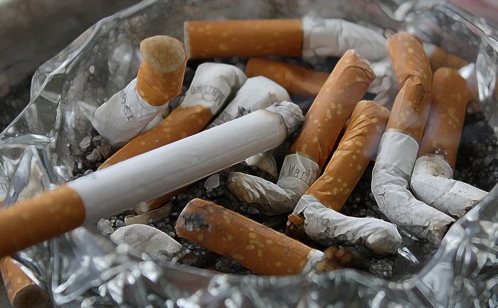A close-up of a glass ashtray brimming with extinguished cigarette butts, highlighting the importance of regular disposal and cleaning to prevent smoke odors in the home.