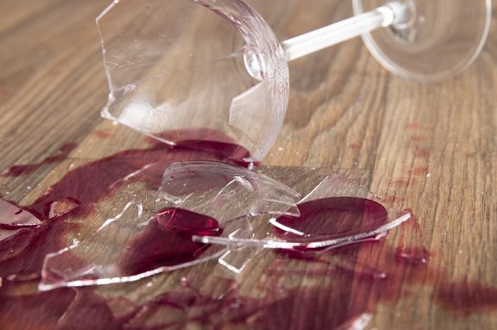 Broken wine glass on wooden surface, illustrating the urgency of swift action in response to spilled wine on carpet.