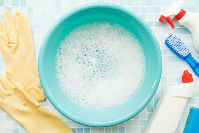 A blue bowl with soap, gloves, and cleaning supplies. Use dish soap and hydrogen peroxide to remove red wine stains from carpet.