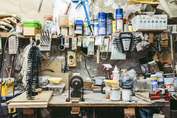 An overfilled workbench in a garage, cluttered with a variety of items and tools, depicting the starting point for decluttering and organizing before a thorough cleaning.