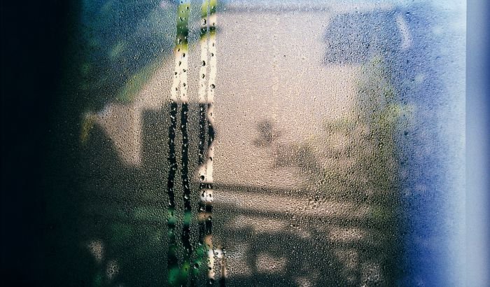 A close-up view of a window with condensation and water droplets, illustrating common household moisture problems.