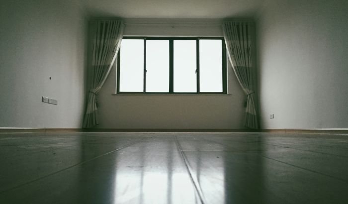 A spacious empty room with natural light streaming in through large windows, highlighting the need for deep cleaning of floors.