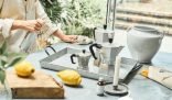 A person using a spray bottle and cloth to clean a kitchen counter with eco-friendly products, including lemons and natural essences, dispelling myths about green cleaning efficacy.