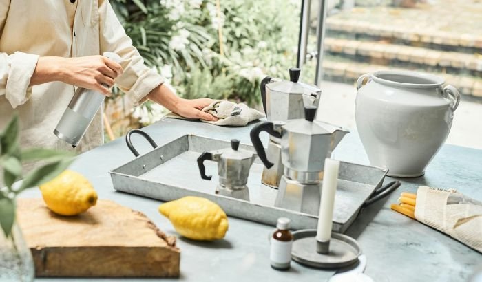 A person using a spray bottle and cloth to clean a kitchen counter with eco-friendly products, including lemons and natural essences, dispelling myths about green cleaning efficacy.