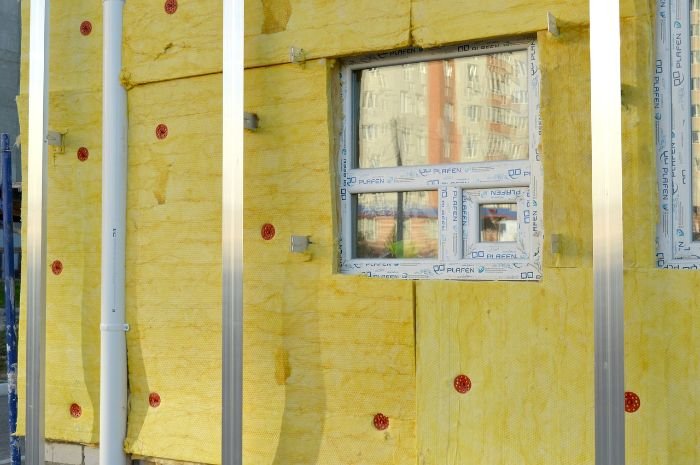Close-up of a building's insulated exterior with yellow fiberglass material and a window, depicting insulation upgrades to reduce home condensation.