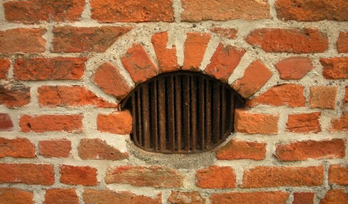 A close-up view of a vintage brick wall with a vent, highlighting the importance of proper ventilation during the cleaning process.