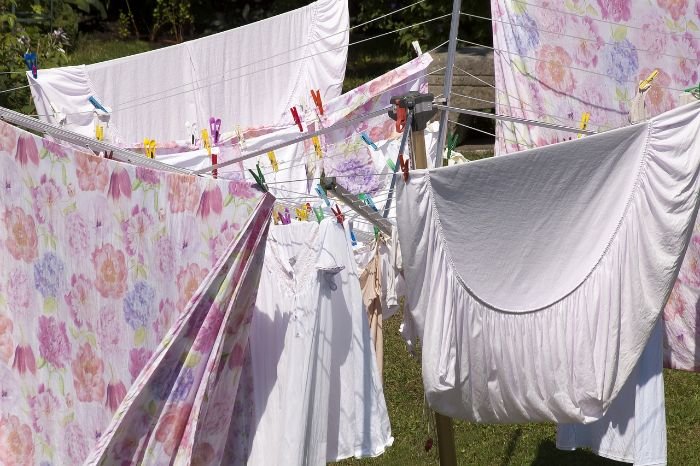 Fresh laundry including bedding and clothes hanging out to dry on a sunny day, clipped with colorful pegs on a clothesline.
