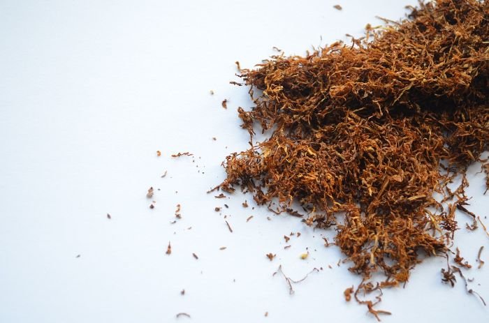 A pile of loose tobacco shreds scattered on a white background, illustrating the raw components of smoke and the difficulty of removing tar and nicotine residues.