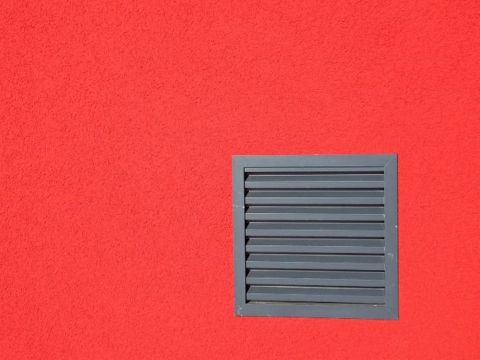 A grey ventilation grid on a vibrant red wall, symbolizing the importance of proper ventilation in a home to prevent condensation.
