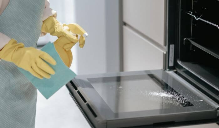 A person wearing gloves meticulously cleaning the interior of an oven, depicting the thorough process of deep cleaning appliances to maintain a high standard of hygiene.
