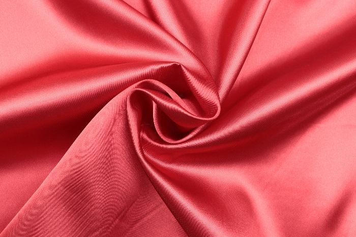 Close-up of a luxurious red silk fabric with a subtle sheen, representing the careful process required for removing oil stains from delicate materials such as silk and wool without causing damage.