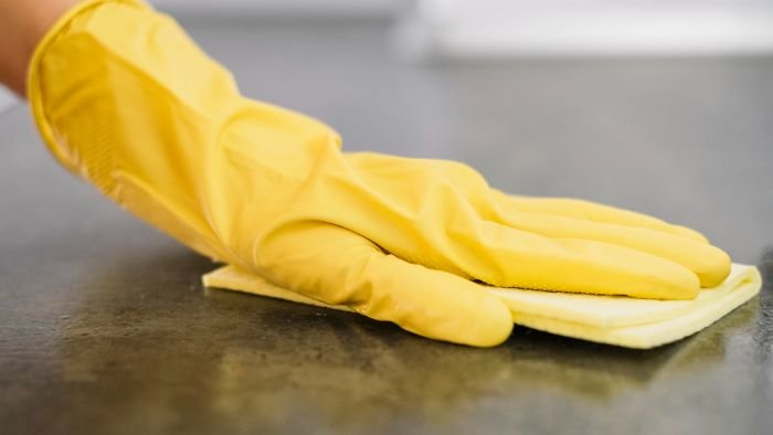 A hand clad in a yellow cleaning glove wipes a surface methodically, depicting the combined efforts of hand hygiene and surface cleaning to ensure a safe and germ-free environment.