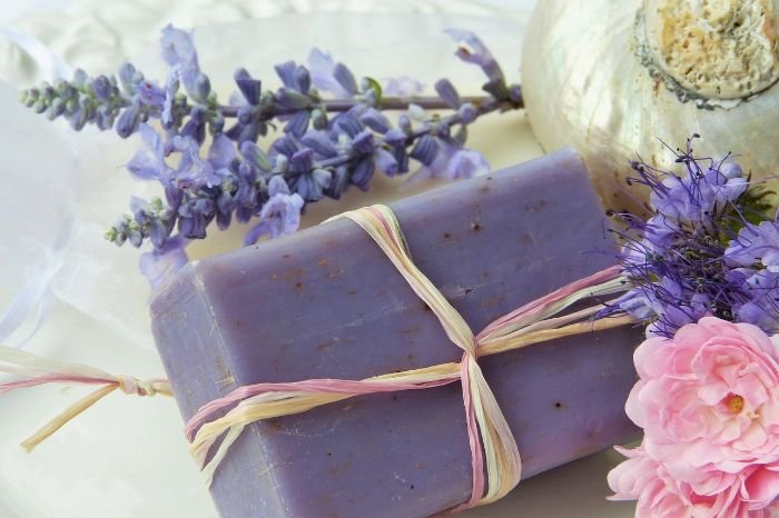 Artisanal lavender soap tied with a raffia ribbon, accompanied by fresh lavender and a pink flower, evoking the essential and fragrant elements of effective hand hygiene practices.