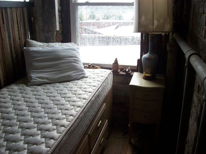 A rustic bedroom setting with a single clean mattress by the window, depicting the choice between natural and chemical cleaning solutions for maintaining a stain-free mattress.