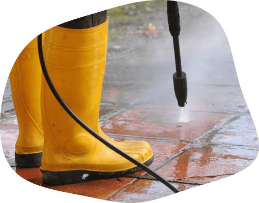 The focused jet of water from a patio cleaning service in progress, with bright yellow boots standing firmly on the freshly cleaned tiles, illustrating the effective and meticulous cleaning technique used to restore patios.