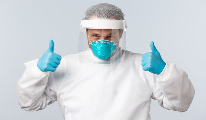 Confident individual giving thumbs up while wearing full protective gear, including a face shield, mask, and gloves, signifying readiness for cleaning tasks.