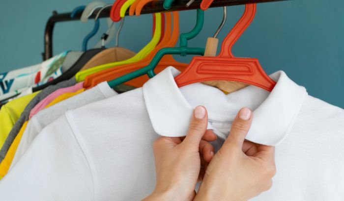 Close-up of hands adjusting a white collared shirt on a hanger among a colorful array of clothes, highlighting the importance of treating and removing oil stains to maintain a clean and presentable wardrobe.