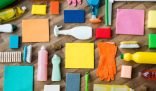 An organized display of various cleaning supplies, including sponges, brushes, gloves, and bottles of cleaners on a wooden surface, representing the importance of safe storage in the household.