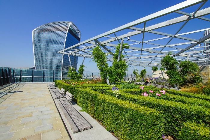 A beautifully landscaped rooftop garden with lush greenery and vibrant flowers, set against the backdrop of a modern skyscraper, exemplifies the transformation of urban spaces into serene green oases by skilled landscaping professionals.