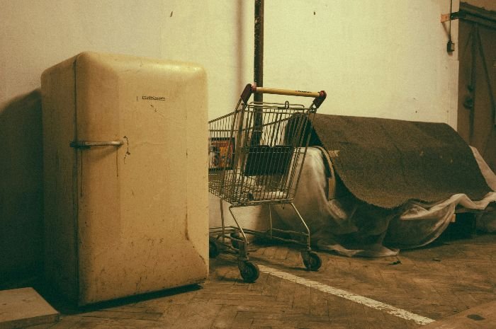 An old and grimy refrigerator alongside a shopping cart, demonstrating the need for thorough fridge cleaning to maintain hygiene and appliance longevity.