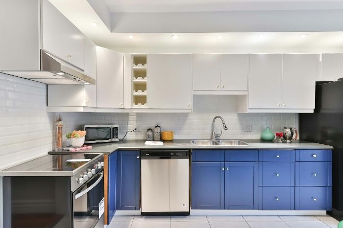 A neat kitchen featuring white cabinets and a striking blue countertop, highlighting the importance of daily cleaning and disinfection to maintain hygiene and prevent contamination.