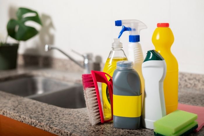 Array of cleaning products on a kitchen counter, highlighting their importance in combating allergens in the home environment for allergy sufferers.