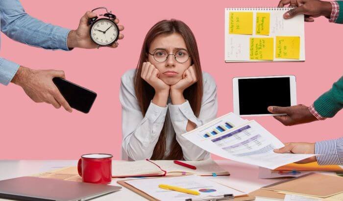 A woman surrounded by various people handing her items such as a smartphone, a clock, documents, and electronic devices, looking overwhelmed at a busy desk, symbolizing a hectic daily schedule.