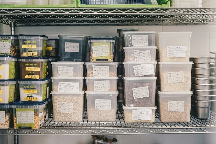 Organized pantry shelves with labeled plastic containers, illustrating the process of decluttering and sorting pantry items.