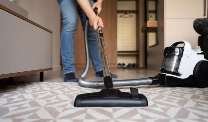 A person using a modern vacuum cleaner to deep clean a patterned carpet, emphasizing the effectiveness of proper equipment in maintaining the cleanliness and longevity of carpets and rugs in a home.