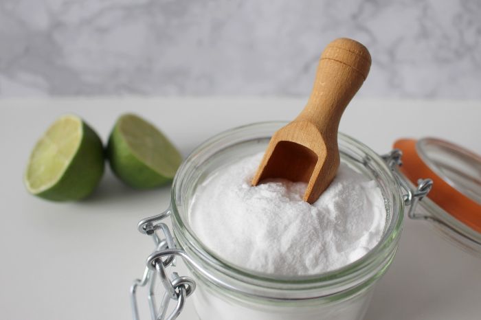 Green Cleaning Tips for Specific Areas in the Home 4 A jar of baking soda with a wooden scoop and lime halves in the background, illustrating natural, eco-friendly cleaning products ideal for dusting and polishing in the living room.