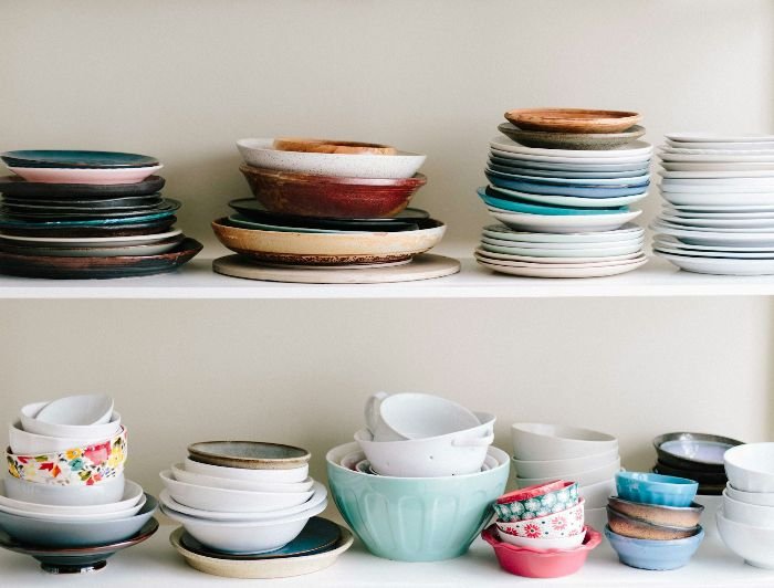An array of neatly organized dishes and bowls on shelves, showcasing diverse styles and colors, illustrating the importance of smart organizational habits in the kitchen to prevent contamination and maintain hygiene.
