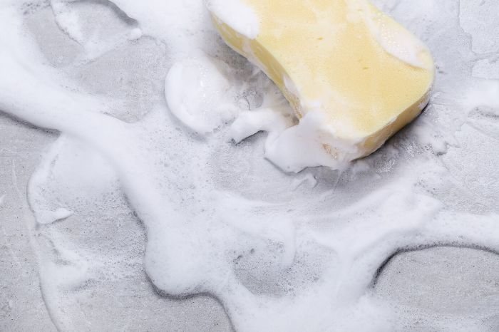 A sponge soaked in soapy water lying on a surface, creating a rich lather that is ideal for pre-treating stains on white fabrics.