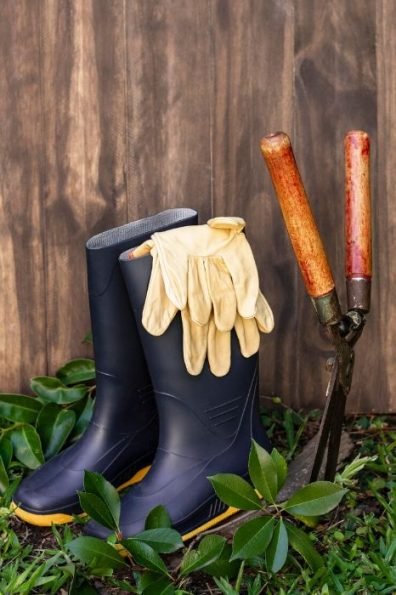 Gardening boots and gloves next to a spade against a wooden backdrop, illustrating essential tools for garden maintenance and landscaping services in Putney, SW15.