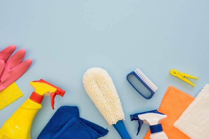 A variety of cleaning tools including spray bottles, microfiber cloths, and brushes laid out on a blue background, illustrating quick cleaning hacks for busy schedules.