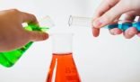 Hands carefully mixing chemicals in laboratory test tubes over a flask containing red liquid, symbolizing the precision and caution required in the safe use of cleaning chemicals.
