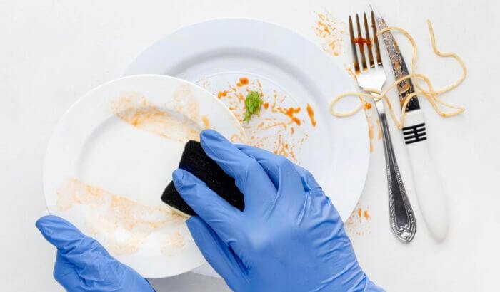 Person wearing blue gloves washing a dirty plate with a sponge, illustrating tips and methods for simplifying your dishwashing routine.