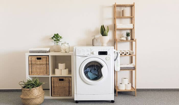 A well-organized laundry room featuring a washing machine, shelves with baskets, plants, and neatly stacked towels, illustrating efficient and streamlined laundry processes.