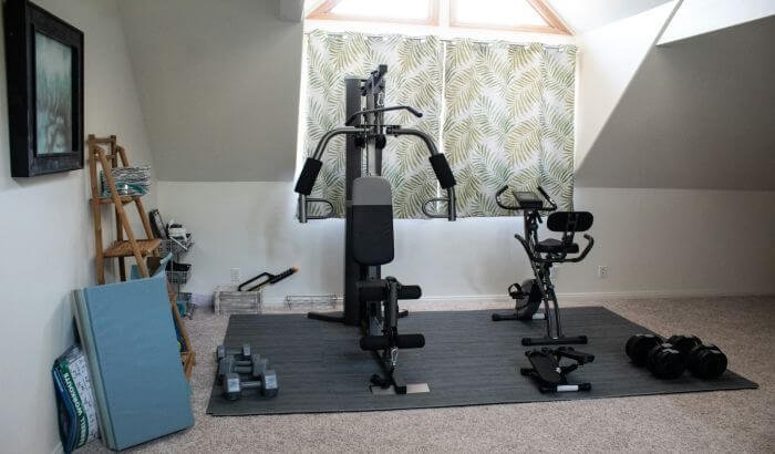 Home gym setup with various exercise equipment, including a multi-gym machine and stationary bike, illustrating best practices for disinfecting your home gym.