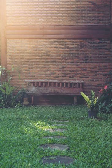 Serene garden setting in Earlsfield with a wooden bench and stepping stones leading through lush green grass, exemplifying well-maintained seasonal garden care.