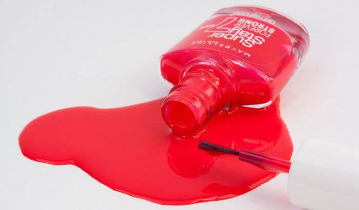 A bottle of red nail polish spilled on a white surface, illustrating the challenge of removing nail polish stains from clothes.