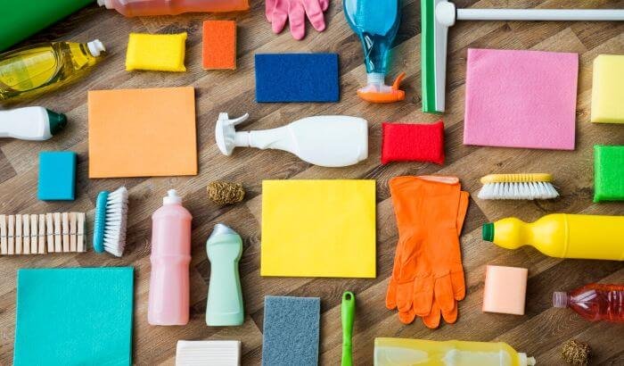 Various colorful cleaning supplies arranged on a wooden surface, illustrating the importance of using child-safe cleaning products in households.