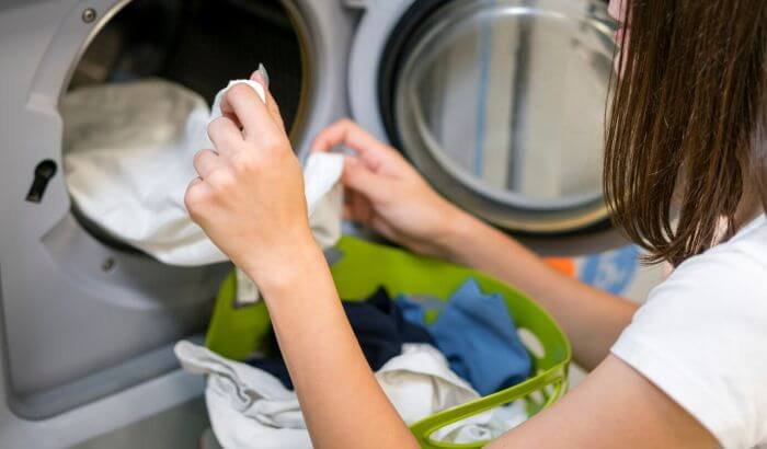 Person loading laundry into a washing machine, emphasizing the importance of regular laundry in maintaining health.