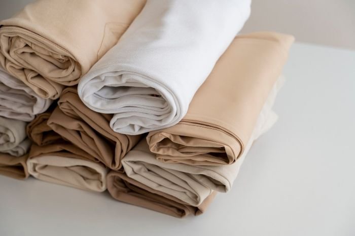 Neatly folded beige and white bedding stacked on a clean surface, demonstrating proper storage techniques to maintain cleanliness.