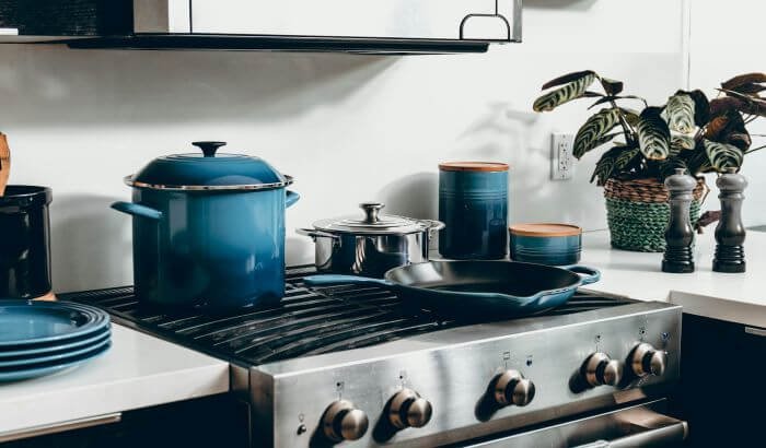 A modern kitchen with blue cookware on the stove, illustrating the importance of removing grease stains from walls and surfaces.