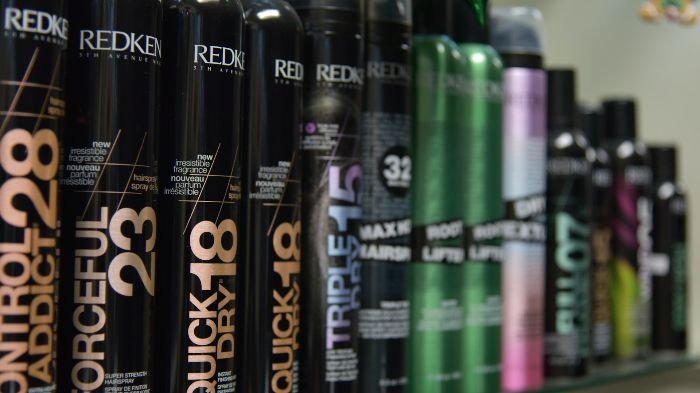 A row of hairspray bottles, including products by Redken, illustrating the use of rubbing alcohol or hairspray for removing nail polish stains from clothes.