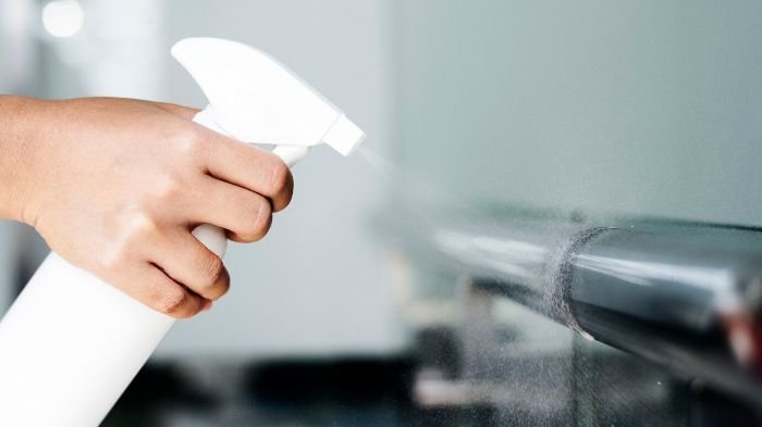 Close-up of a hand using a spray bottle to disinfect a metal railing, illustrating the importance of choosing non-toxic disinfectants for safe cleaning practices in a home gym.