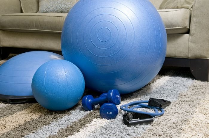 A collection of blue fitness equipment including an exercise ball, hand weights, and resistance bands on a carpeted floor, illustrating a step-by-step guide for cleaning and disinfecting home gym equipment.