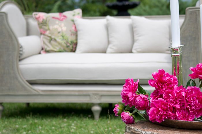 A beautifully arranged outdoor seating area with vibrant pink flowers in the foreground, representing the focus on summer garden maintenance tasks to keep the garden healthy and attractive during the warmer months.